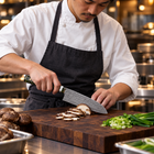 A Japanese chef using the Ibuki 7-Inch Santoku Knife on a wooden cutting board in a professional kitchen