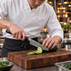 A Japanese chef using the Shiden Utility Knife on a wooden cutting board in a professional kitchen
