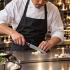 A Japanese chef using the Shingen Utility Knife on a titanium cutting board in a professional kitchen