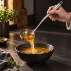 Rounded-handle soup ladle serving soup into a ceramic bowl