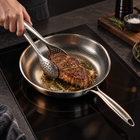 Perforated serving tongs turning steak in the silver Okura hammered pan